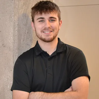 Link, young man in black polo leaning again a cement pilar, profile page